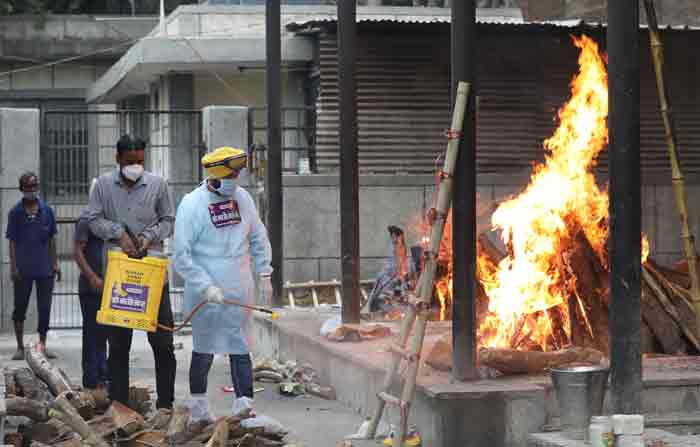 Voluntarios indios desinfectan cerca de una hoguera en llamas durante un funeral masivo de víctimas de covid-19 en un crematorio en Nueva Delhi, India, el 18 de mayo de 2021. Foto: EFE