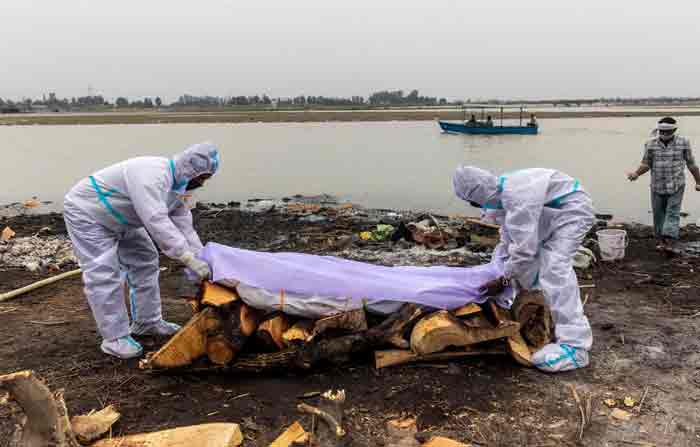 Hombres con trajes de protección ponen una tela blanca sobre el cuerpo de una persona que murió de covid-19 antes de su cremación en la ribera del río Ganges, en Garhmukteshwar. Foto: REUTERS