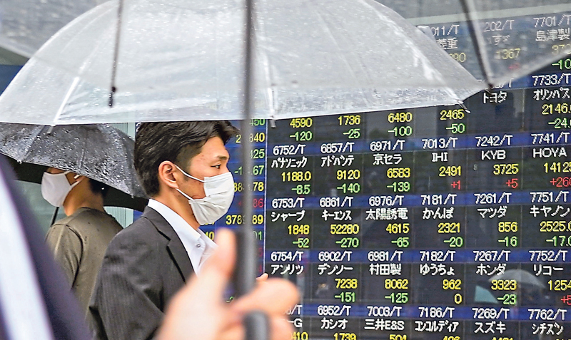 Transeúntes pasan delante de un tablero que muestra varios datos de la Bolsa de Valores de Tokio.
