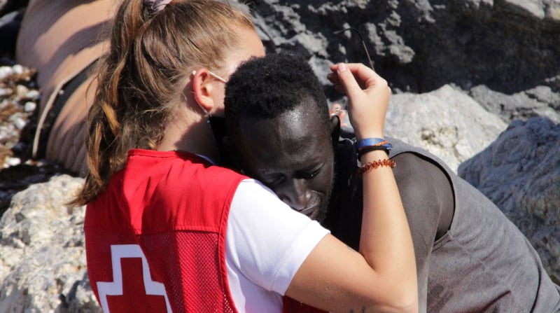 Luna, una trabajadora de la Cruz Roja y un migrante que logró cruzar uno de los espigones fronterizos de Ceuta este martes 18 de mayo del 2021 se abrazan. Foto: EFE