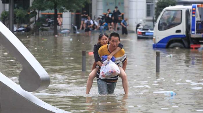 Un hombre lleva a una mujer en la carretera inundada después de que las lluvias récord retrocedieran en la ciudad de Zhengzhou en la provincia de Henan. Foto: EFE
