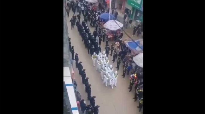 Cuatro sospechosos con mascarilla y con trajes de protección, de los que colgaban sus fotografías y nombres, tuvieron que desfilar el 27 de diciembre frente a una numerosa multitud en la ciudad de Jingxi. Foto: Captura