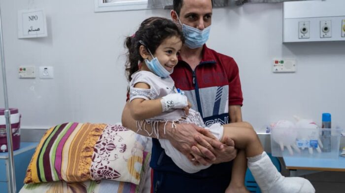 Palestina, agosto de 2021. Hala, de cuatro años, es cargada por su padre, Mohammed, antes de que la operen. El tratamiento de las lesiones por traumatismos puede ser un desafío en la Franja de Gaza bloqueada. Foto: Virginie Nguyen Hoang 