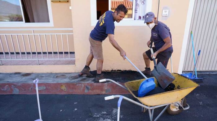 Dos hombres limpian de ceniza volcánica el frente de su casa en el municipio palmero de Tazacorte. Foto: EFE