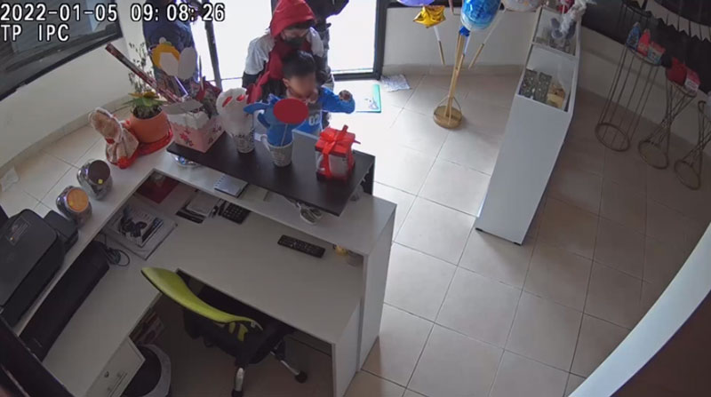 En la cámara de seguridad quedó registrado el momento en el que una persona toma el rostro del niño y le indica objetos en el local que fue robado. Foto: Captura de pantalla