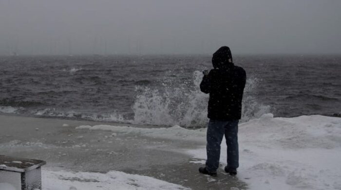 Un peatón se detiene para tomar fotografías de las olas rompiendo en Fan Pier, en Boston, Massachusetts, EE.UU., este 29 de enero de 2022. Foto: EFE
