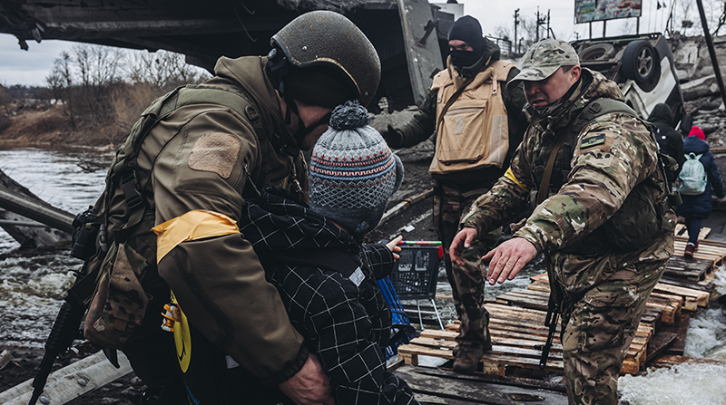 Unos soldados ayudan a cruzar el río a un niño, a 7 de marzo de 2022, en Irpin (Ucrania). Foto: Europa Press