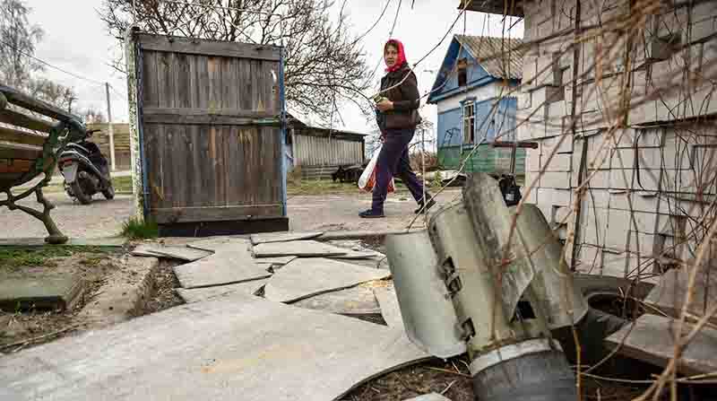 Una mujer camina junto a una parte de un misil en el patio de una casa privada en la aldea de Kukhari, en la zona de Kiev, Ucrania. EFE