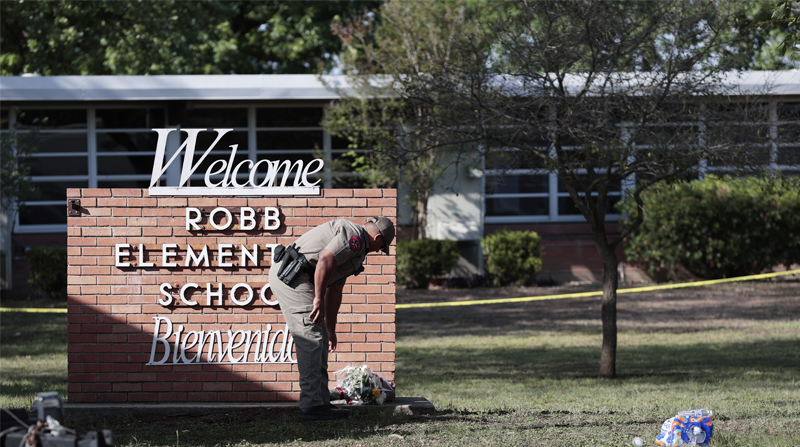Un policía estatal de Texas coloca flores al pie del letrero de la Escuela Primaria Robb mientras los investigadores continúan trabajando en la escena de un tiroteo masivo en la escuela que mató a 19 niños y dos adultos según el gobernador de Texas Greg Abbott en Uvalde, Texas. Foto: EFE