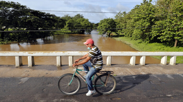 Un hombre pasa en bicicleta junto a un río crecido después del paso de las lluvias, en la ciudad de San Juan y Martínez. Foto: EFE