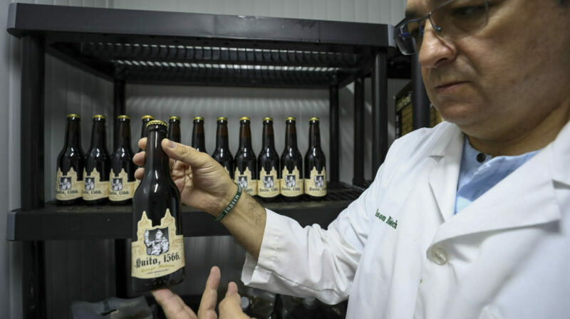Javier Carvajal, investigador y profesor de la Pontificia Universidad Católica de Ecuador (PUCE), sostiene una botella de la cerveza 'Quito 1566', el 18 de agosto de 2022, en Quito (Ecuador). Foto: EFE.