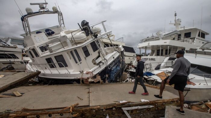 Dos hombres miran los destrozos causados por el huracán en botes atracados en Fort Myers. Foto: EFE.