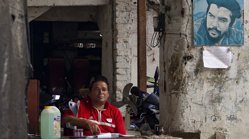 Un hombre cuida un parqueadero de autos, en donde se ve una foto del Che Guevara. Foto: EFE.