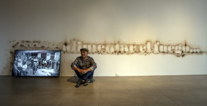 El artista Fabiano Kueva junto a la instalación ‘Alimentar el fuego’, que incluye un esténcil quemado con gas. Foto: DIEGO PALLERO / EL COMERCIO