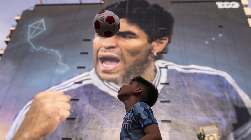 Un niño juega fútbol cerca del mural en honor a Diego Armando Maradona, realizado por el artista Martín Ron, considerado como unos de los mejores muralistas del mundo. Foto: EFE