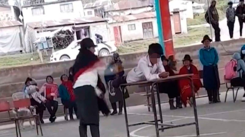 Momento en el que un niño se recuesta sobre una mesa y recibe el castigo físico en público. Foto: Captura de pantalla