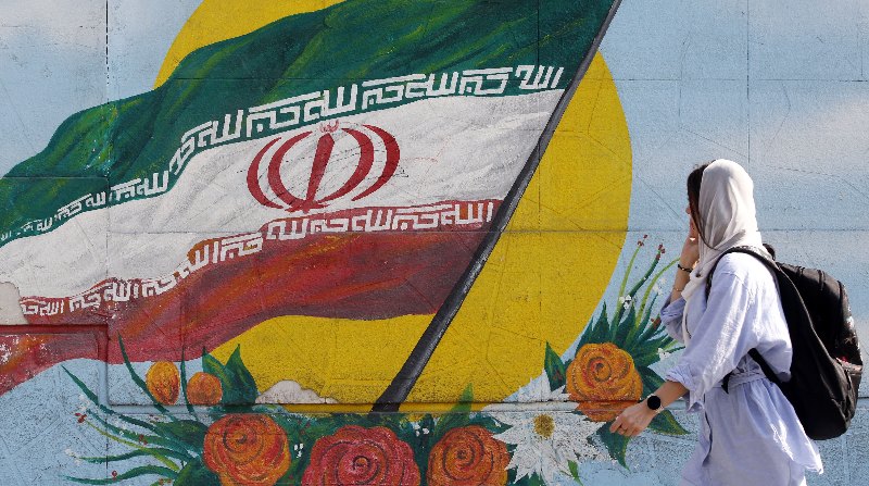 Una mujer cubierta su cabeza con velo pasa delante de un grafiti con la bandera iraní en Teherán, ciudad que ha sido escenario de manifestaciones. Foto: EFE