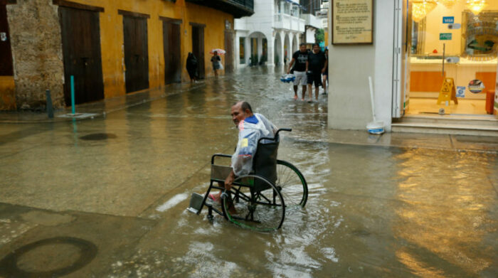 Un hombre en silla de ruedas transita, por una calle inundada, en Cartagena de Indias (Colombia). Foto: EFE.