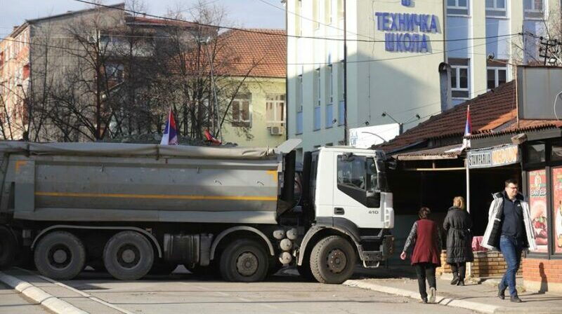 Habitantes de Mitrovica, en Kosovo, caminan delante de camiones que bloquean la ruta antes de que el Gobierno serbio haya anunciado el desmantelamiento de esas barreras. Foto: EFE.