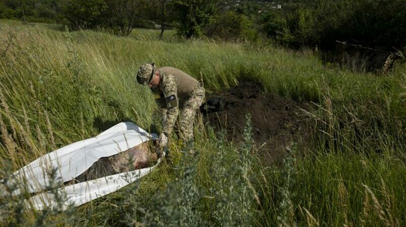 Un soldado ucraniano recoge los cuerpos de dos soldados rusos que estaban sepultados en las afueras de Járkov. Foto: EFE.