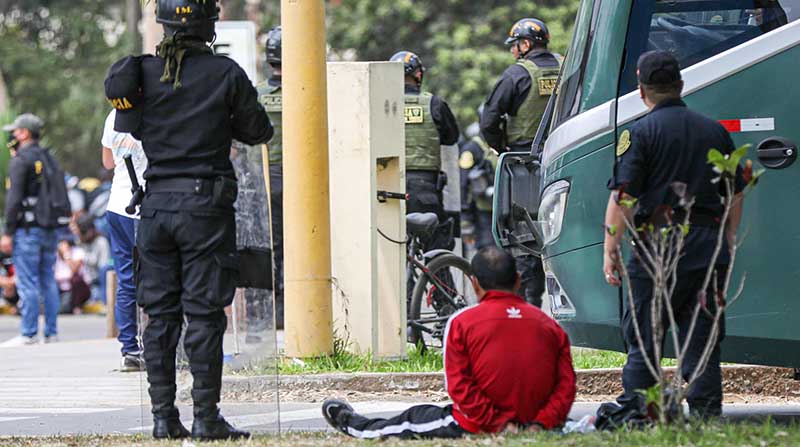 Integrantes de la Policía Nacional de Perú vigilan a una persona detenida en el campus de la Universidad Nacional Mayor de San Marcos, este sábado 21 de enero en Lima (Perú). Foto: EFE