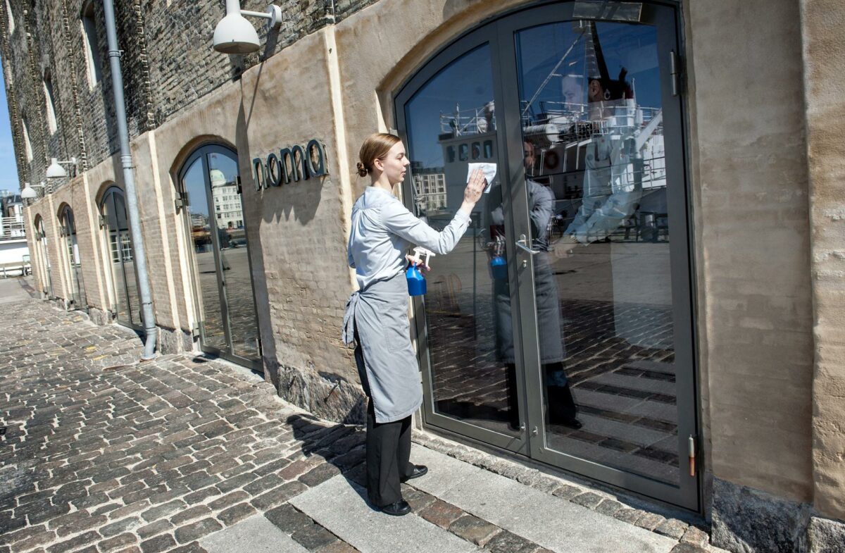Un miembro del equipo del restaurante Noma en Copenhague limpia una puerta del local. Foto: EFE