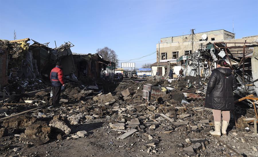 Dos ucranianos se encuentran entre los escombros en un mercado local dañado por los bombardeos rusos en la ciudad de Shevchenkove. Foto: EFE.