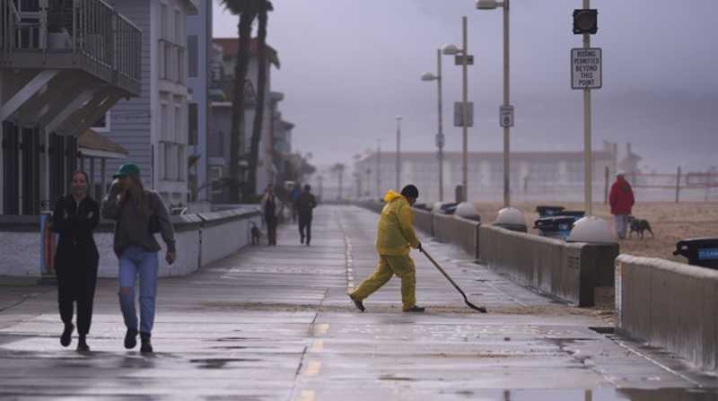 Vista de un trabajador despejando una vía de agua y arena durante una tormenta de lluvia en una playa de Los Ángeles. Foto: EFE / Archivo