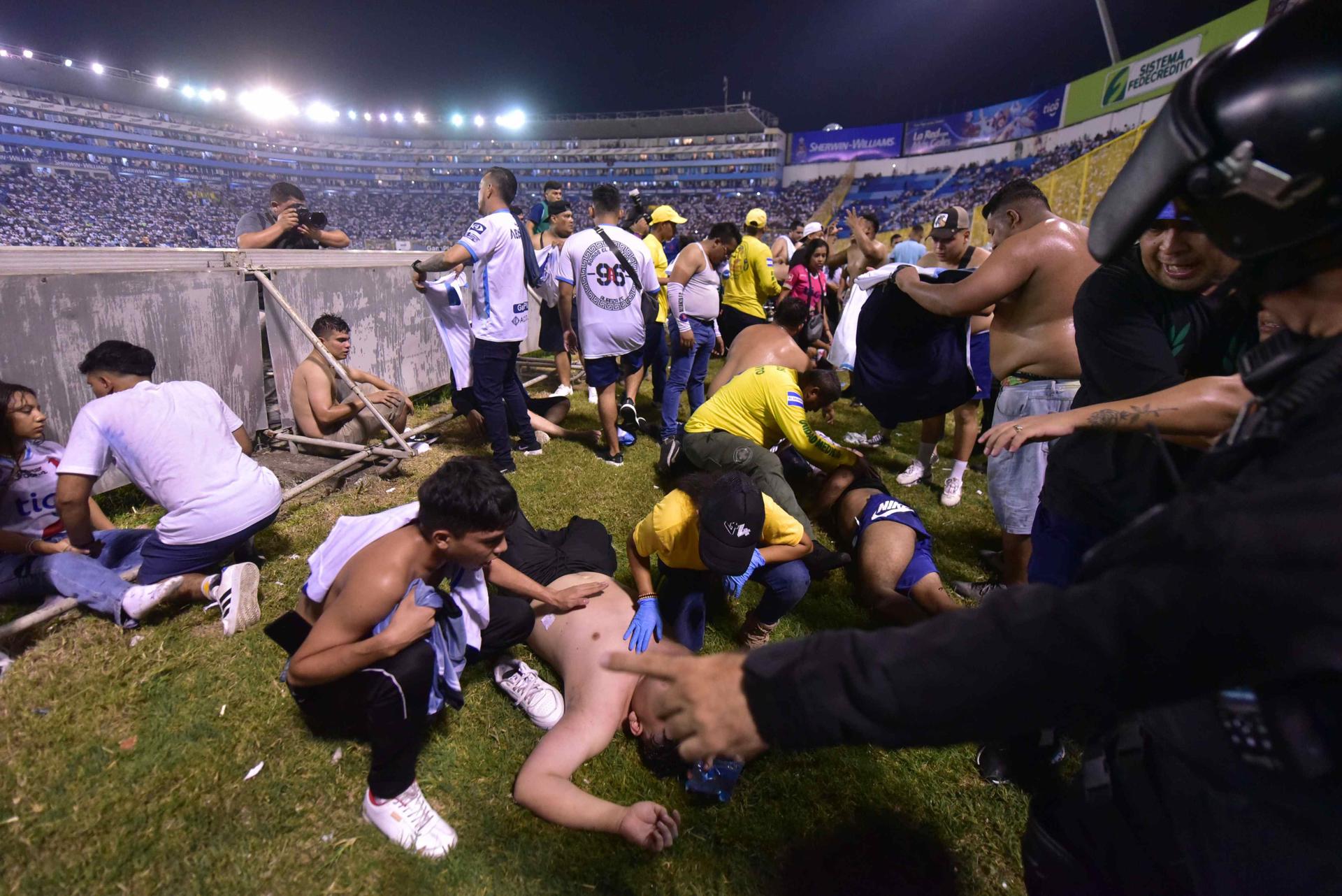 Fanáticos auxilian a personas durante una estampida en el Estadio Cuscatláán previo a un partido de la Liga Mayor, en San Salvador. Foto: EFE.