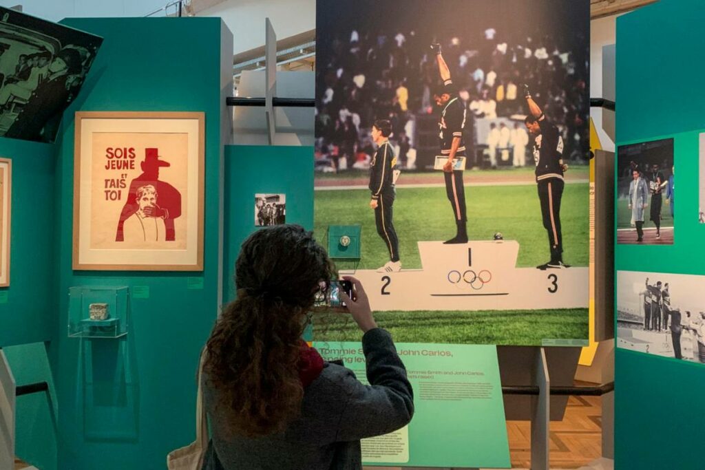 Una mujer hace una foto en la exposición 'Olimpismo, una historia del mundo' del histórico momento del saludo del Poder Negro protagonizado por Tommie Smith y John Carlos en los Juegos Olímpicos de México de 1968. Foto: EFE